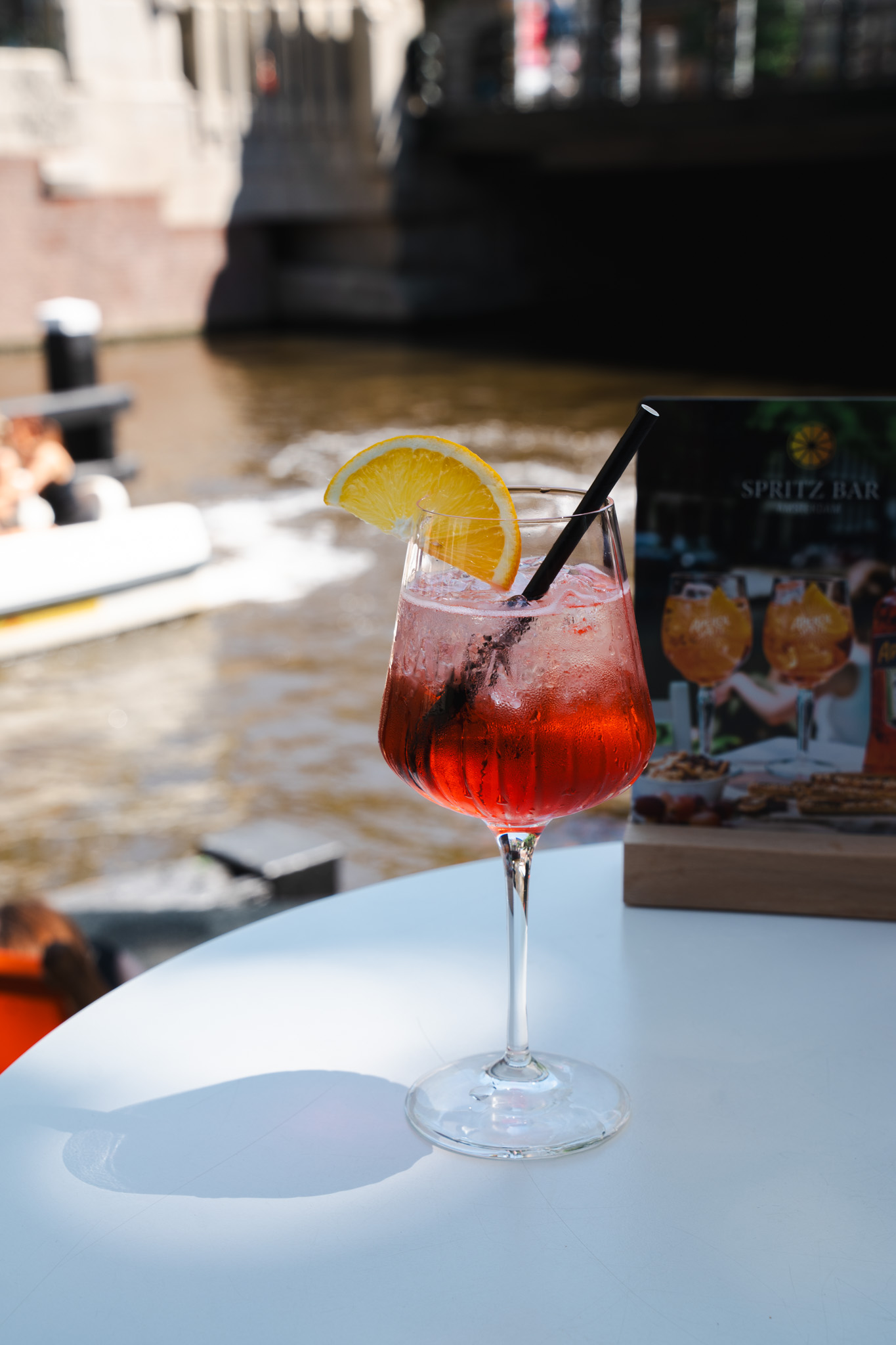Red Campari Spritz on table with Amsterdam canal and boat behind