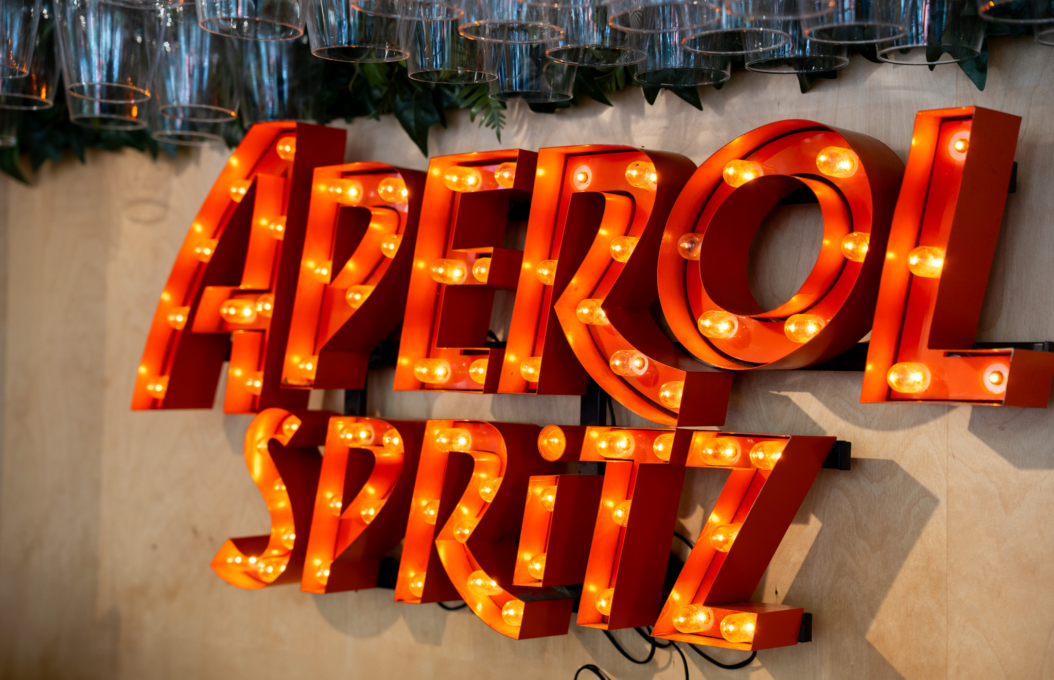 Aperol Spritz illuminated marquee letters on wall with glasses above