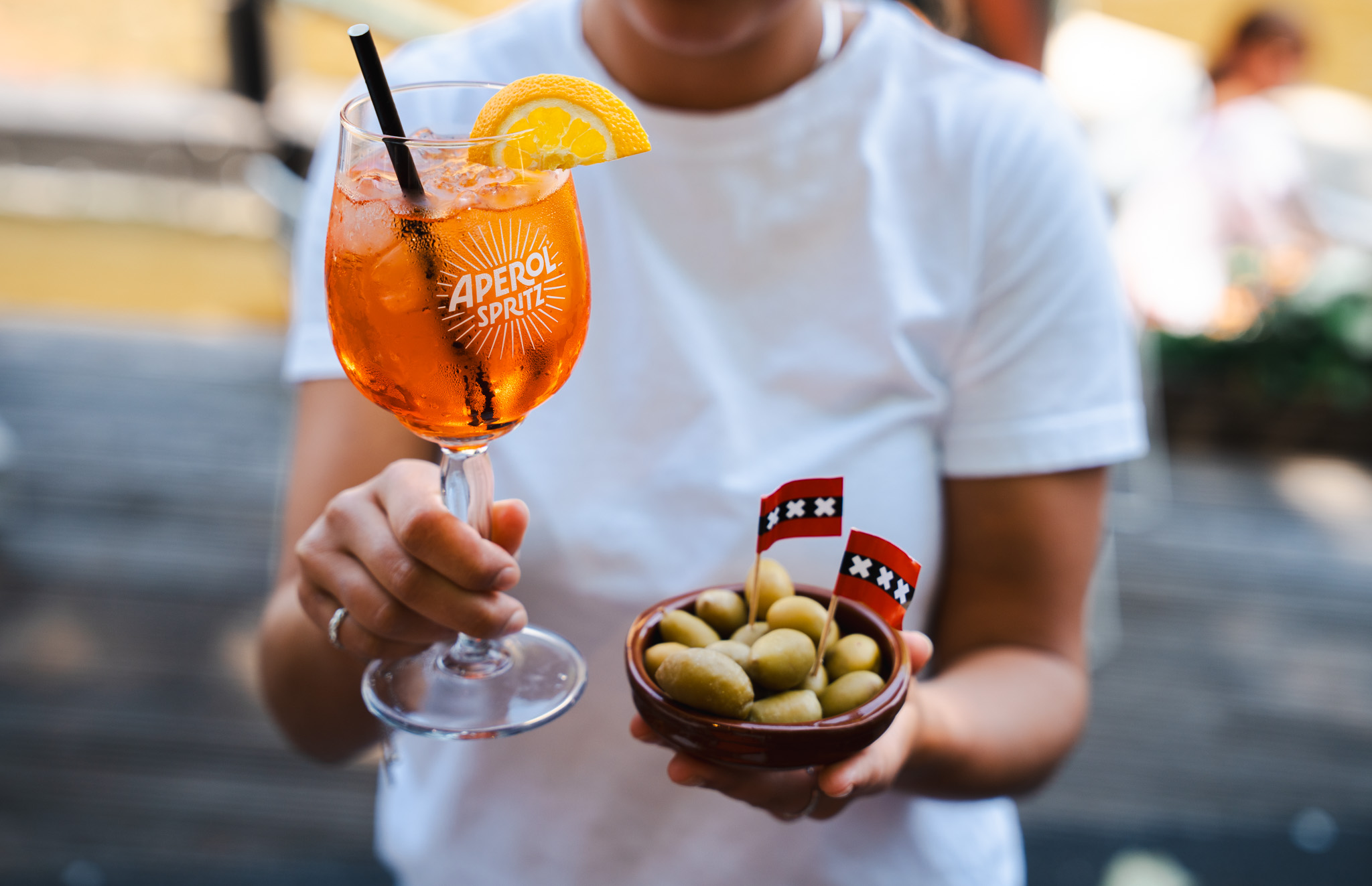 Person holding Aperol Spritz glass and bowl of olives with Amsterdam flags